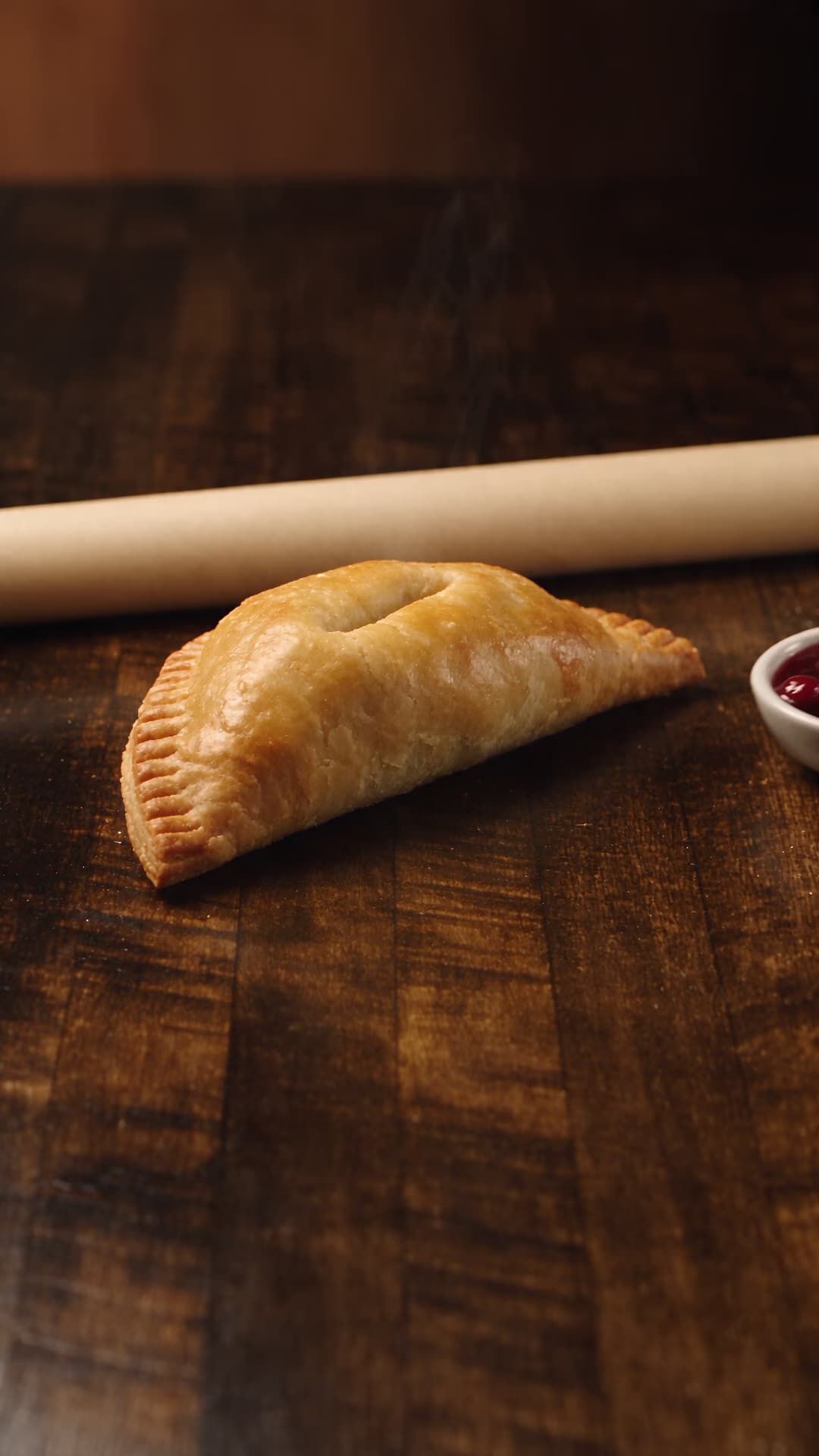 Savory hand pie beside cranberry relish on walnut wood.